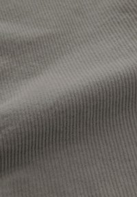 Grijze corduroy stof met een verticale ribbelstructuur. Het materiaal is zacht met een subtiele glans. De ribbels benadrukken golvende patronen.