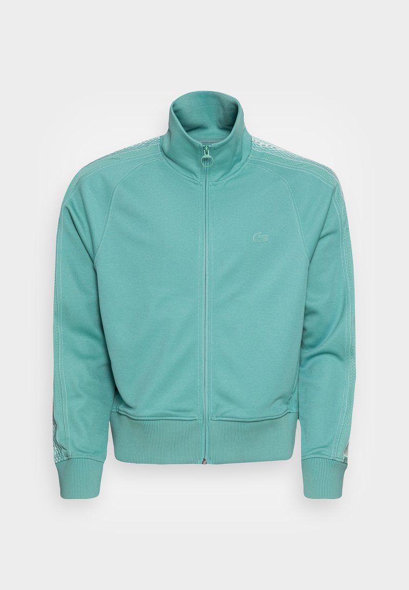 Turkooise trainingsjack met volledige ritssluiting, geribbelde manchetten en zoom, hoge kraag, subtiel logo op de borst en sierstiksels op schouders en mouwen.