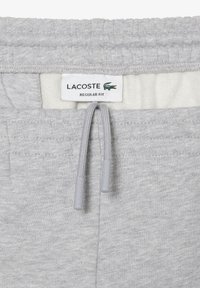 Gray sweatpants made of soft fabric with an elastic waistband, featuring a drawstring and Lacoste logo tag indicating regular fit.