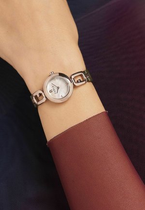 Montre ronde en argent avec un cadran en nacre et un bracelet en cuir vert, présentant des accents métalliques et un design de bracelet lié.