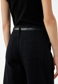 Mustat korkea vyötäröiset housut, joissa on tekstuuri, ja joissa on kaksi takataskua sekä ohut musta nahkavyö.