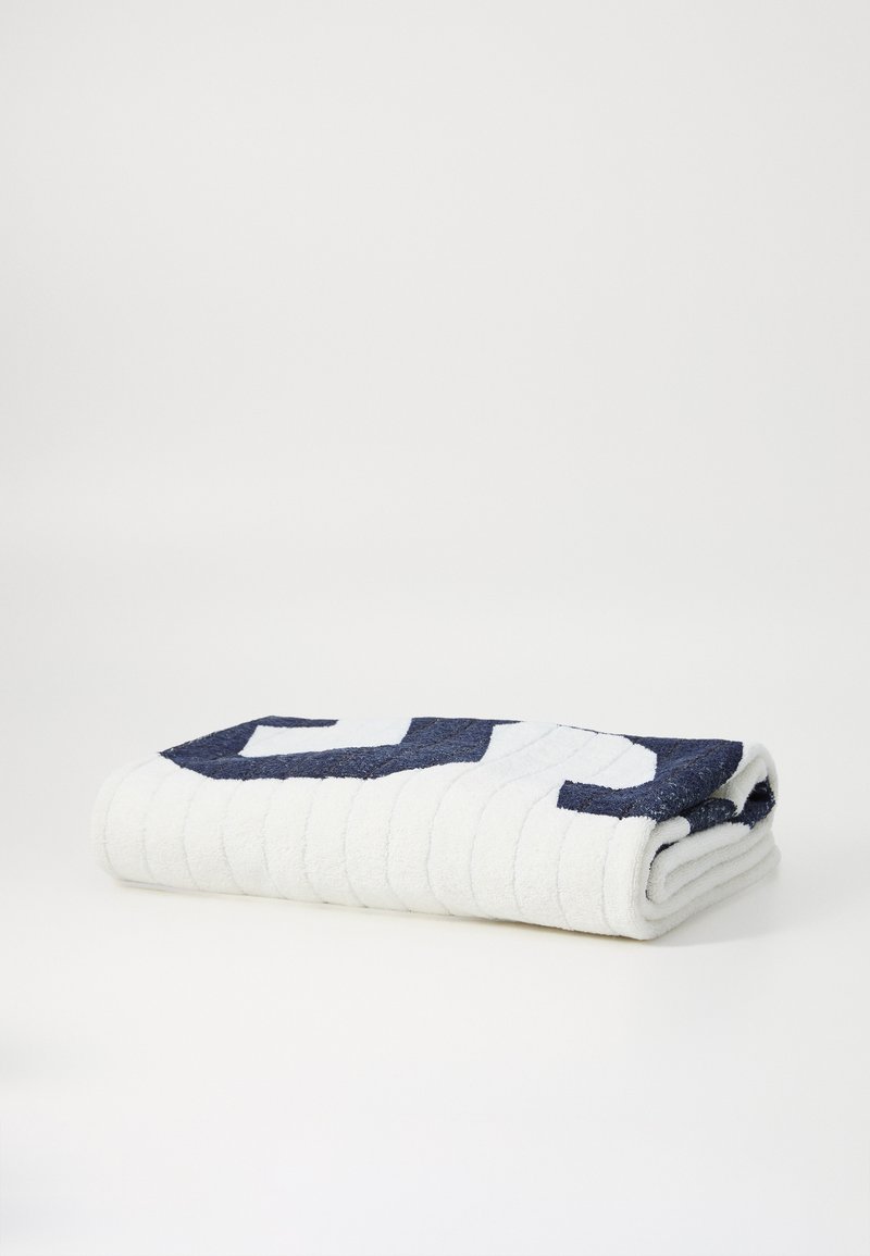 Fehér törölköző sötétkék geometriai mintával, puha tapintású, szépen felgöngyölítve, finom bordázott részletekkel az élein.
