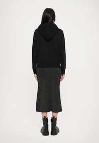 Black hoodie with a front kangaroo pocket, paired with a gray knitted midi skirt and black ankle boots with chunky soles.