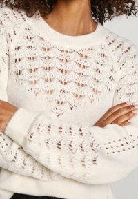 Pull tricoté couleur crème avec un motif à maille lâche, col rond côtelé et manches larges ornées de détails subtils semblables à de la dentelle.