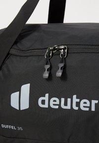 Borsone nero con chiusura a zip, dotato di doppi tirazip e logo impresso. Realizzato in tessuto resistente, progettato per la portabilità.