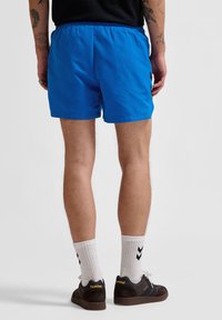 Blå simshorts med elastisk midja, tillverkade av lätt material. Stilade med en avslappnad passform, parat med mörka sneakers och vita strumpor.