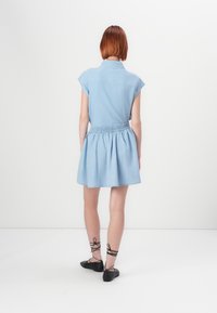 Light blue denim dress with short cap sleeves, elastic waist, and a flared skirt. Worn with black lace-up flats. Back view.