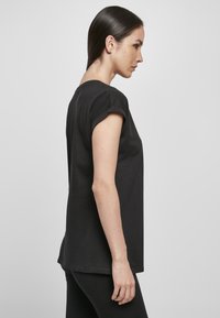 Black short-sleeve t-shirt made from smooth cotton jersey. Features a curved hem and rolled sleeves, displayed on a model in profile.
