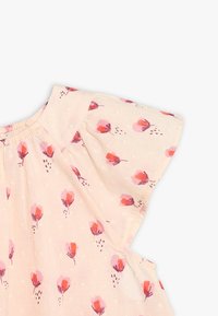 Lichtroze blouse met fluttermouwen, voorzien van een bloemmotief in tinten van roze en paars, en met gestructureerde stipdetails.