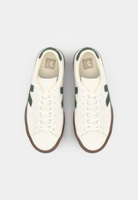 White sneakers with green accents, featuring a smooth leather upper, round toe, flat laces, and a gum rubber sole. Logo on the tongue.