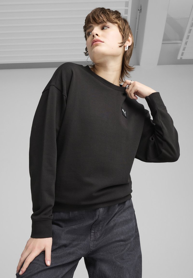 Schwarzer Sweatshirt mit rundem Halsausschnitt und gerippten Bündchen, mit einem kleinen weißen Logo auf der Brust. Glatte Textur, lockerer Schnitt.
