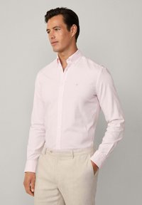 Light pink button-up shirt made of cotton, featuring a classic collar and long sleeves, paired with light beige pants for contrast.
