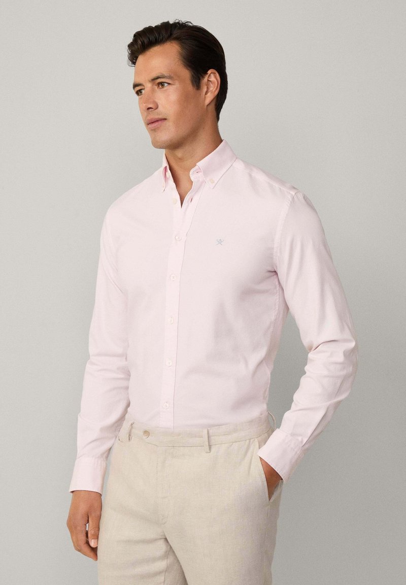 Chemise boutons-pression rose clair en coton, avec un col classique et des manches longues, assortie à un pantalon beige clair pour le contraste.