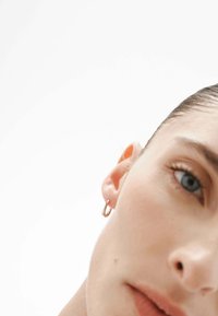 Aro de oro en la oreja de un modelo, con una superficie lisa y brillante. El modelo tiene un fondo neutro, con un enfoque en primer plano en el aro.