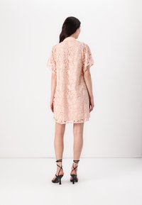 Lace-kjole i myk ferskenfarge, med korte ermer og blomsterpatter. Inntrukket midje med avslappet passform, kombinert med svarte sandaler med stropper.