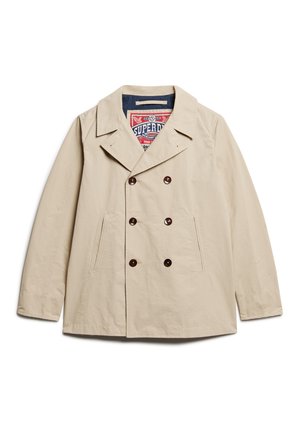Beige dobbelbrystet jakke lavet af letvægtsstof. Har store brune knapper, to sidelommer og en marineblå foring med branding.