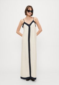 Rochie maxi de culoare crem cu detalii în nuanța navy, bretele subțiri ajustabile, decolteu adânc în formă de V și buzunare laterale, fabricată dintr-un material ușor.