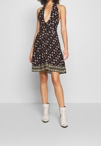 Czarna sukienka na szyję z głębokim dekoltem w kształcie litery V, wzorem kwiatowym i zdobionym dołem. Noszona z srebrnymi botkami w print wężowej skóry.