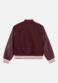 Burgundijas bomberis ar ādas piedurknēm, vilnas ķermeni, rozā un baltas svītrainas ribu aproces un jostu. Gluda tekstūra un brīvs piegriezums.