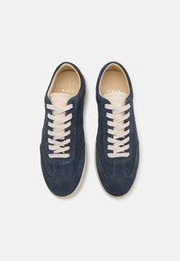 Navy suede sneakers with beige laces, rounded toe, and subtle stitching details. Features a cream-colored interior and logo on the tongue.