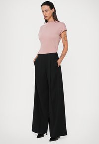 Top ajustado de color rosa claro con mangas cortas, combinado con pantalones anchos de tiro alto en color negro que cuentan con bolsillos y una textura elegante.