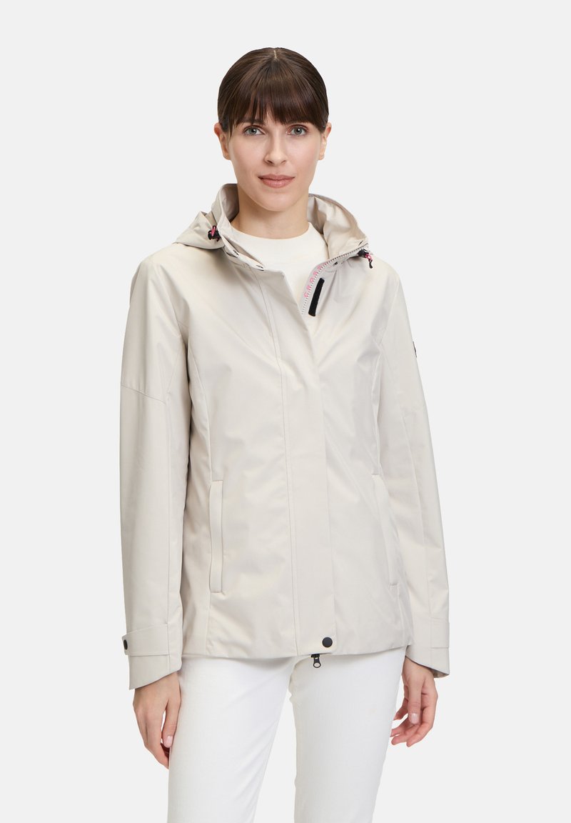Veste imperméable beige clair avec capuche, dotée de poches zippées, de cordons de serrage réglables et d'une texture lisse.