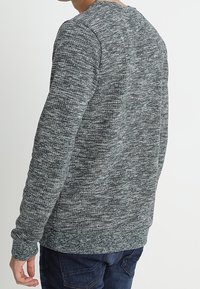 Suéter gris texturizado con mangas largas, cuello redondo y puños acanalados. La tela presenta un patrón mezclado de hilos claros y oscuros.