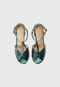 Green metallic heeled sandals with crisscross pleated design, open toe, ankle strap, and circular hardware detail on the side.