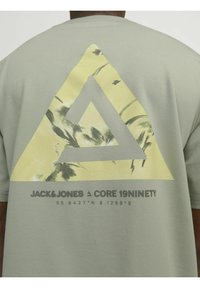 Kortærmet, lys grøn t-shirt med et stort gult trekantgrafik med abstrakt design og tekst nederst.