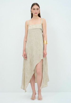 Beige pitkä maxi-mekko, jossa on neliönmuotoinen pääntie, ohuet hihnat ja korkea halkio. Kangas on pehmeä, ja siinä on pieni kiilto.