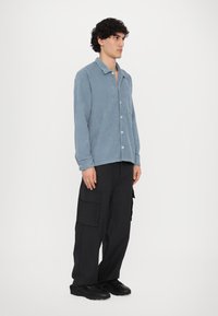 Light blue corduroy shirt with a button-up front, collar, and long sleeves, paired with black cargo pants and black sneakers.