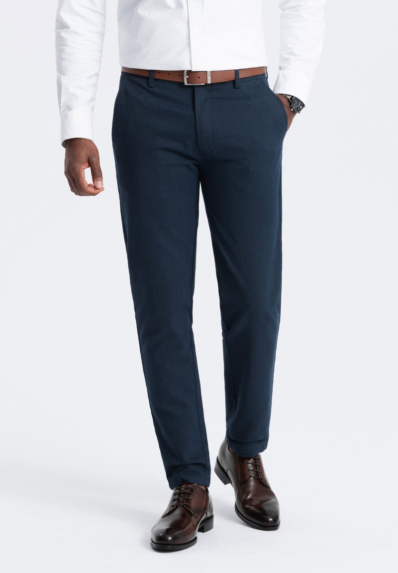 Pantaloni blu navy in taglio slim, realizzati in tessuto leggero, con frontale piatto, tasche laterali e una cintura in pelle marrone.