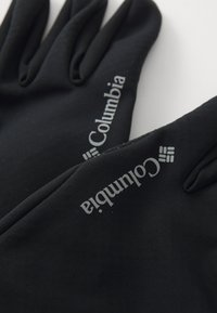 To svarte Columbia-hansker med trykket merkevare-navn og logo på baksiden av hendene, lagt på en hvit overflate.