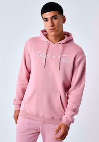Sudadera con capucha rosa hecha de tela suave, con un bolsillo frontal y texto bordado en blanco "Project x Paris". Diseño minimalista.