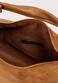 Καφέ σουέντ τσάντα με ταμπά χερούλι από συνθετικό δέρμα. Το εσωτερικό είναι επενδεδυμένο με απαλό ύφασμα, διαθέτει φερμουάρ και εσωτερική ετικέτα με το λογότυπο της μάρκας.