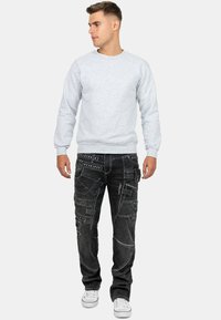 Felpa grigia in cotone con polsini e orlo a coste, abbinata a jeans cargo neri con più tasche e borchie decorative. Sneakers bianche.