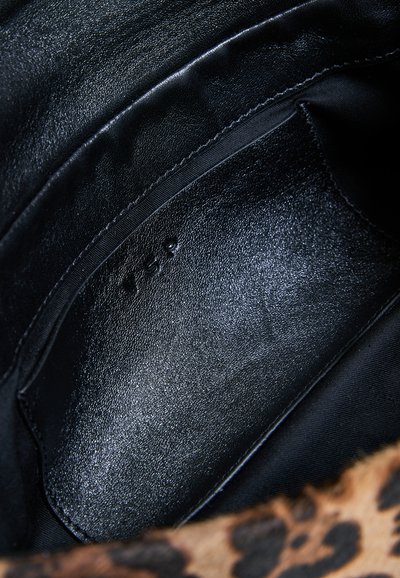 Gros plan d'une poche intérieure en cuir noir avec un texte embossé "YSP" sur un fond en tissu à imprimé léopard.