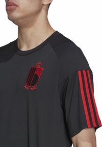 T-shirt athlétique noir avec un blason brodé rouge et des accents de bandes rouges sur les manches. Confectionné dans un tissu lisse et léger.