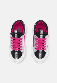 Valkoiset ja mustat tennarit, joissa on vaaleanpunaiset nauhat ja yksityiskohdat, jotka ovat varustettu tekstuuripinnoilla, paksulla pohjalla ja näyttävillä logoyksityiskohdilla.