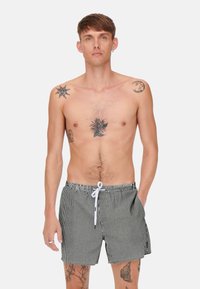 Schwarz-weiß gestreifte Badeshorts mit einem elastischen Bund, Zugbandverschluss und seitlichen Taschen. Verfügt über eine leichte Stofftextur.