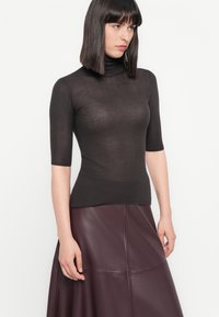 Prilagođeni, rebrasti turtleneck top u tamnosmeđoj boji. Kratke rukave, lagani materijal s suptilnom teksturom. Uparen s burgundi kožnom suknjom.
