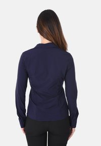 Camicia blu navy con maniche lunghe e colletto, caratterizzata da un design aderente e una texture morbida, con cuciture visibili sul retro.