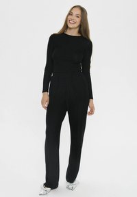 Schwarzes Langarmshirt mit schmaler Passform, kombiniert mit schwarzen weiten Hosen. Das Outift zeichnet sich durch eine glatte Textur und eine schlichte, klassische Silhouette aus.