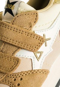 Sneaker con tomaia in canvas beige, accenti in suede marrone, cuciture bianche e dorate, e chiusure in Velcro con design a stella e triangolo.
