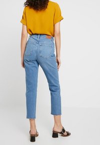 Vaaleansiniset korkeavyötäröiset farkut, joissa on kulutettu helma, takataskut ja vaalea nahkaluukku. Yhdistetty sinapinkeltaiseen paitaan ja mustiin korkokenkiin.