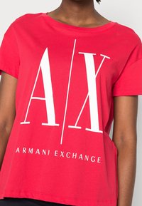Czerwona bawełniana koszulka z krótkim rękawem, z dużym białym nadrukiem logo "A/X" oraz napisem "ARMANI EXCHANGE" na dole.