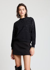 Sweat-shirt noir orné d'embellissements argentés éparpillés, col rond et manches longues. Associé à une mini-jupe noire et des bottes montantes jusqu'aux genoux.