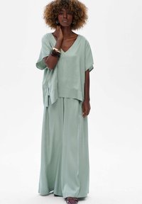 Jasnozielony, oversize'owy top i spodnie o szerokich nogawkach z miękkiego, lejącego się materiału. Prosty dekolt w serek, luźny krój i subtelny połysk.