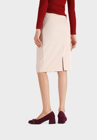 Gonna a matita beige con spacco sul retro, abbinata a scarpe con tacco a blocco in suede bordeaux caratterizzate da un accento decorativo in metallo.