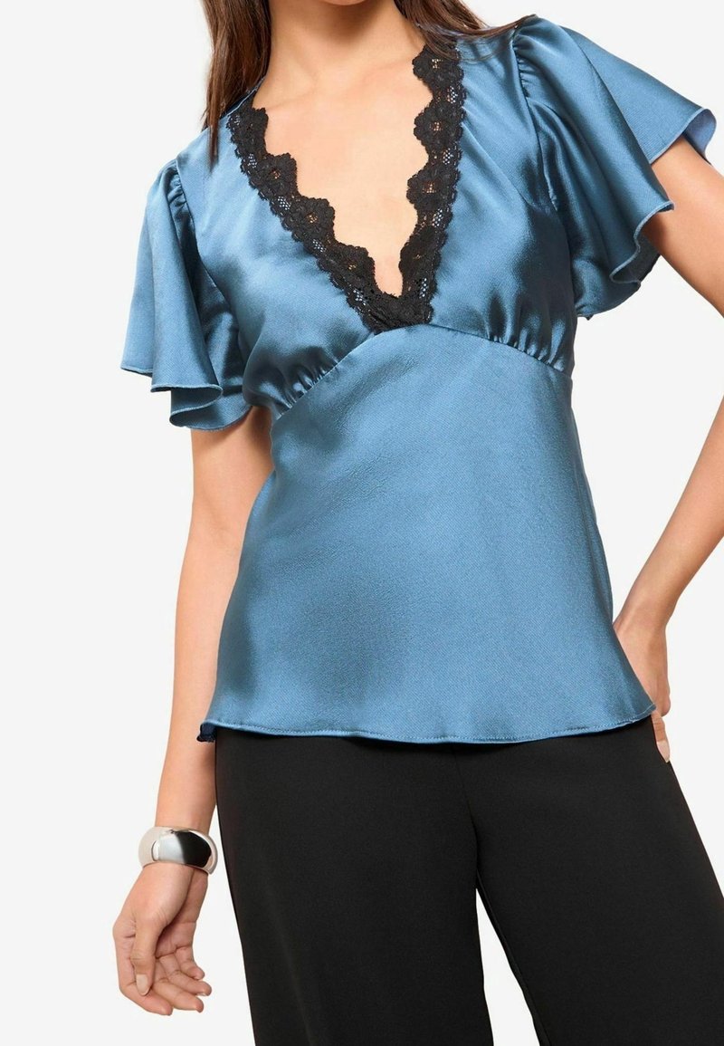 Blå satinblus med svart spets V-ringning och utställda ärmar, med en mjuk textur och avslappnad passform, i kombination med svarta byxor.